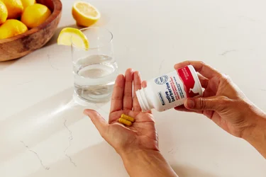 A hand pouring two capsules of NativePath Native Berberine into their hand with a glass of water and lemons in the background