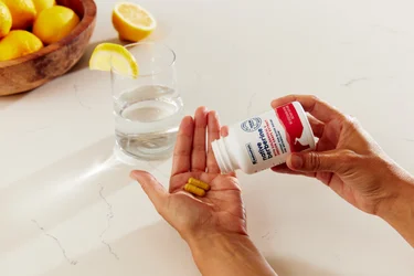 A person pouring two capsules of Native Berberine from the bottle in their hand. A glass of water in the background.