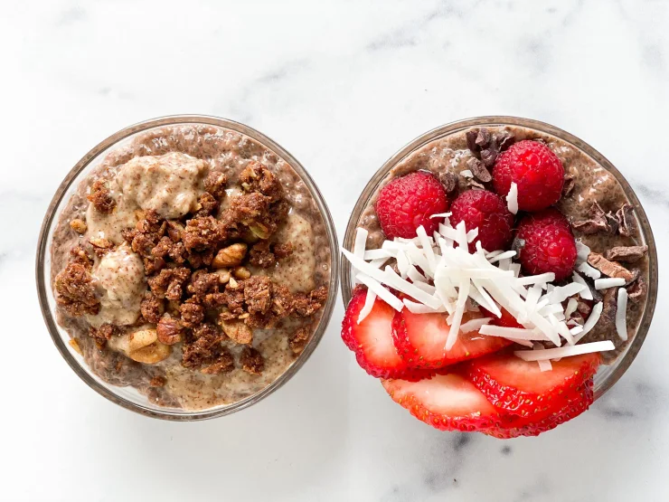 A bowl of Chocolate Chia Seed Pudding with berries and coconut flakes and a bowl of Chocolate Chia Seed Pudding with Native Nola paleo granola