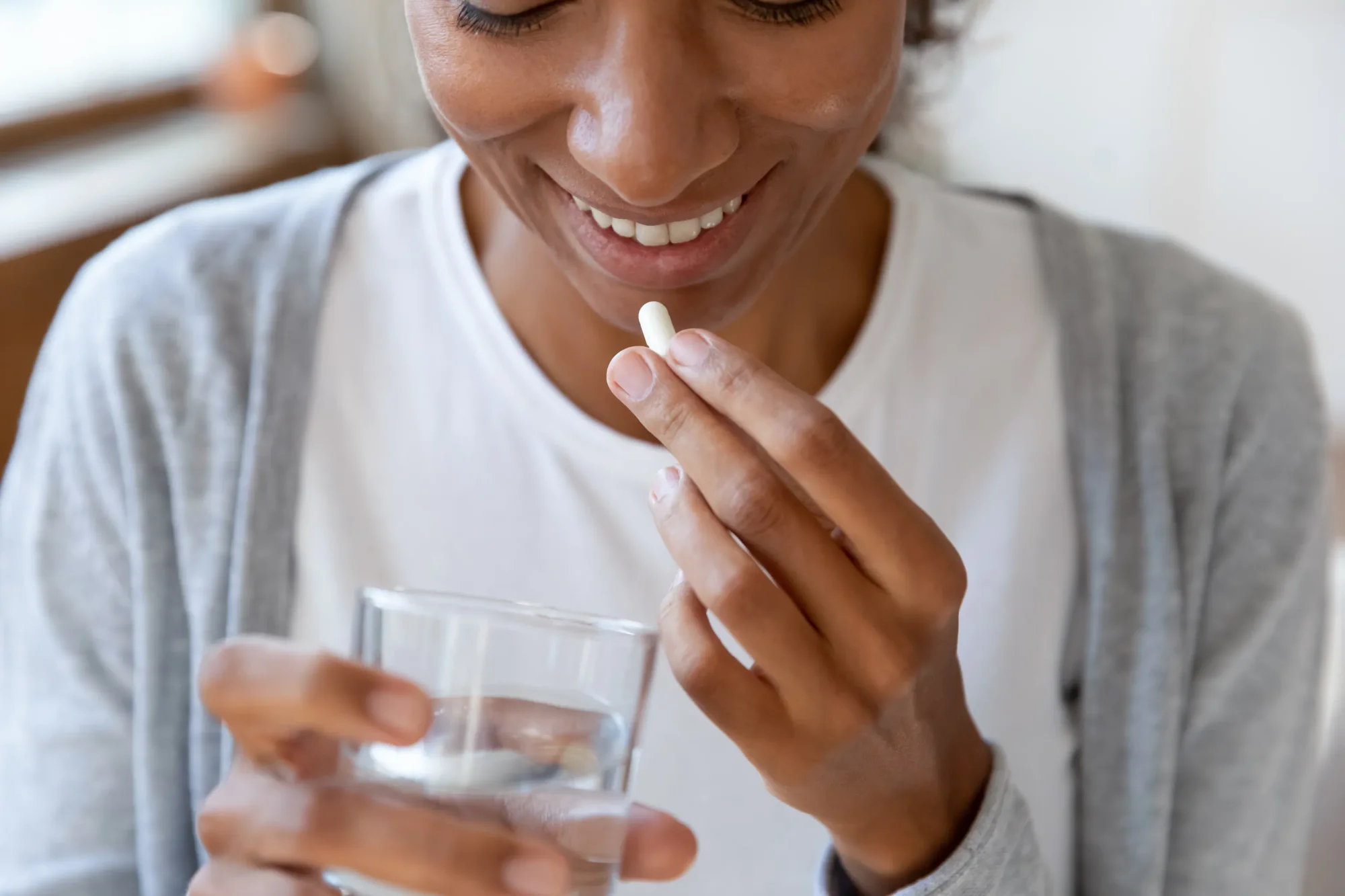 Close up happy young African American young woman taking a probiotic capsule with a glass of fresh water. Gut health concept.