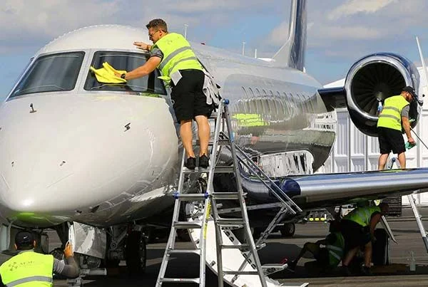 Crew in high-visibility vests washing an aircraft on the ramp from ladders