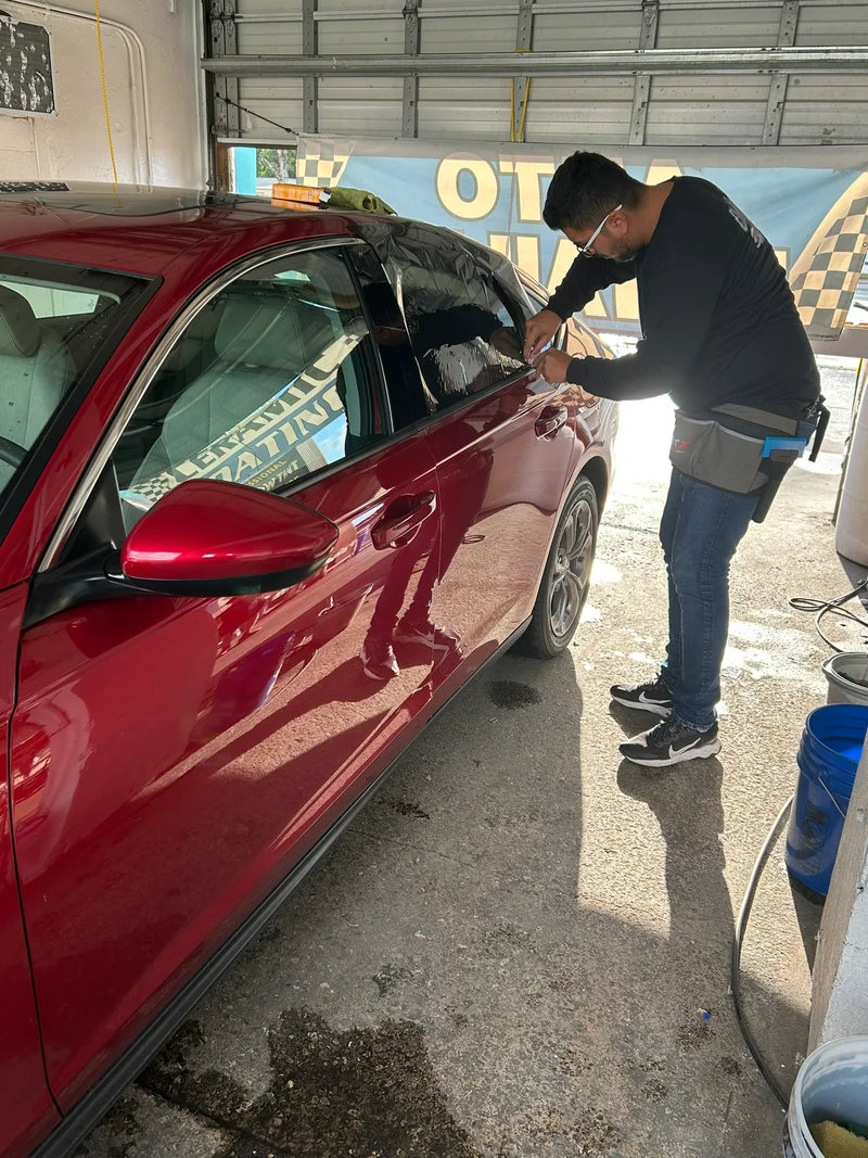 Technician applying window tint to a red sedan