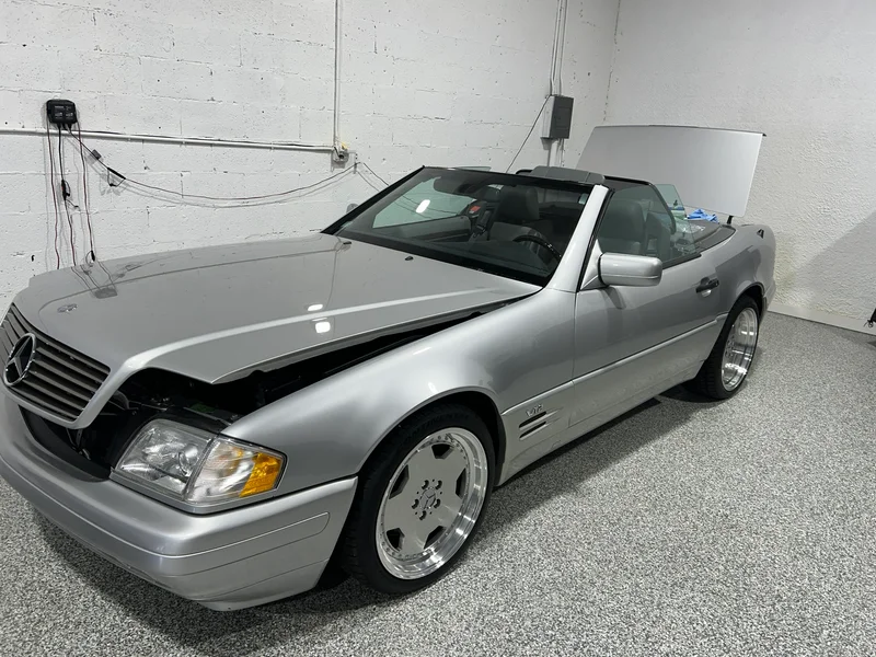 Silver convertible with its hood open in the prep garage