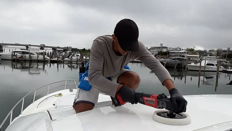 Technician polishing a white boat deck with a rotary polisher at the marina