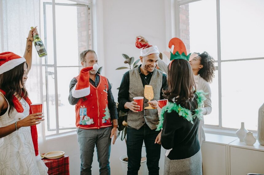 A group of people wearing festive Christmas outfits and hats, smiling and celebrating together in a joyful atmosphere.