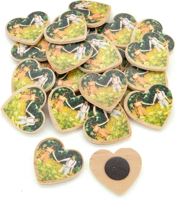 Heart-shaped wooden magnets with a pastoral couple image in a lush green field. One magnet flipped, showing a black magnetic back, conveying a romantic and rustic theme.
