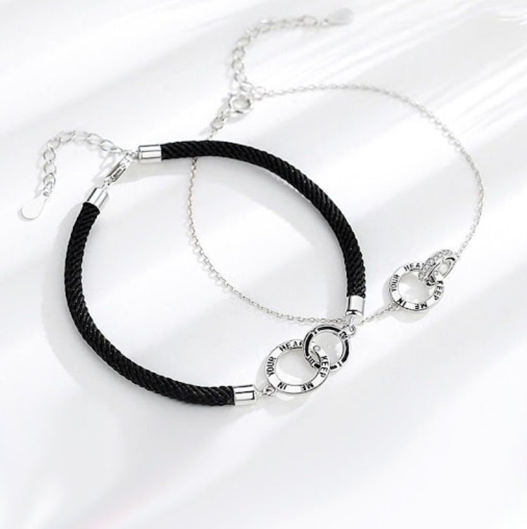 Two bracelets featuring black cord and silver charms, elegantly displayed side by side.
