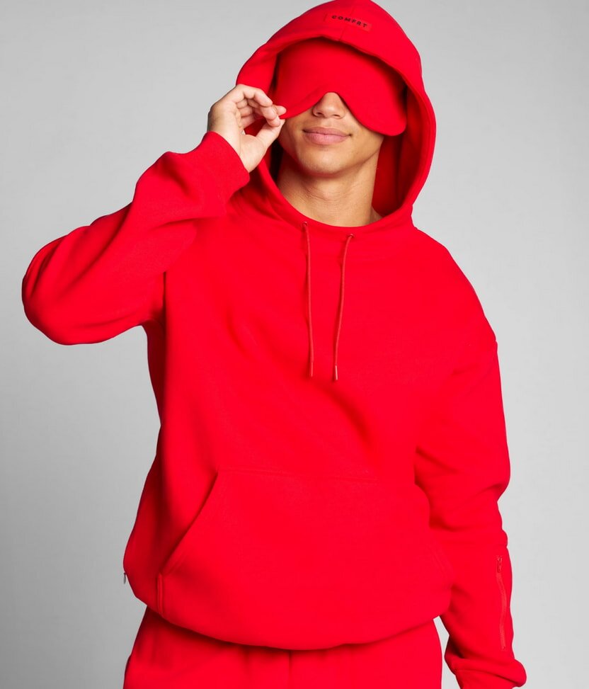 A man dressed in a red hoodie and matching sweatpants stands casually.