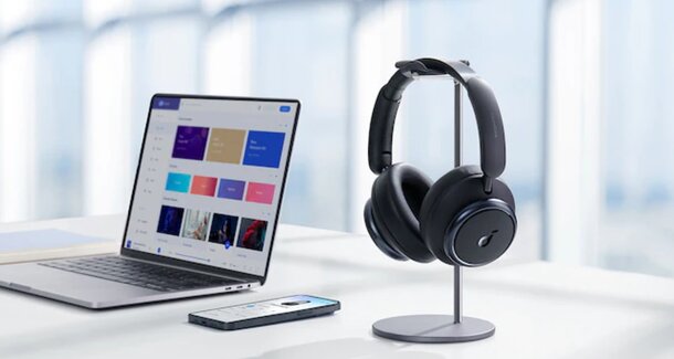 A laptop and headphones sit on a desk beside a smartphone, creating a workspace for productivity and communication.