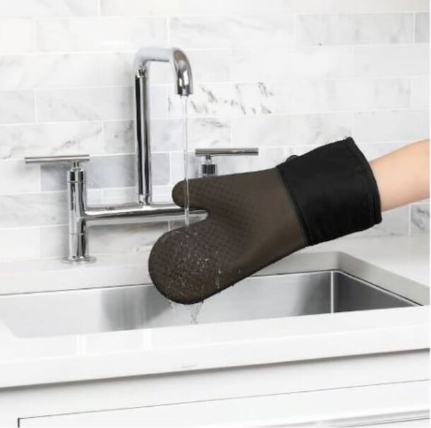 A person in a kitchen wearing a black oven mitt, preparing to handle hot cookware.