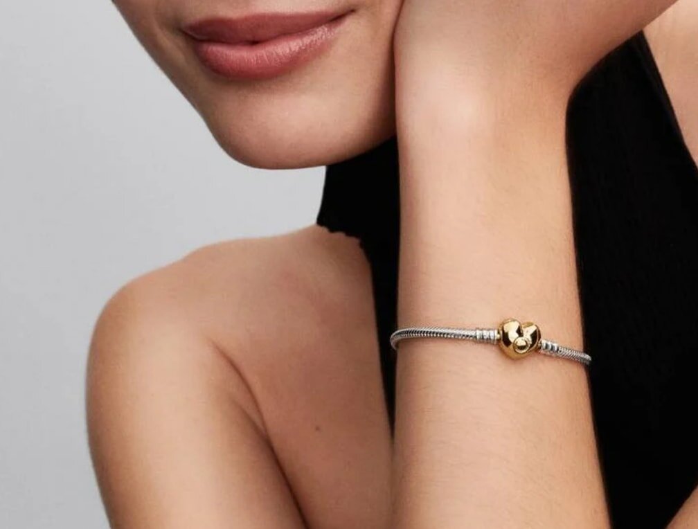A woman showcases a bracelet adorned with a heart charm on her wrist.