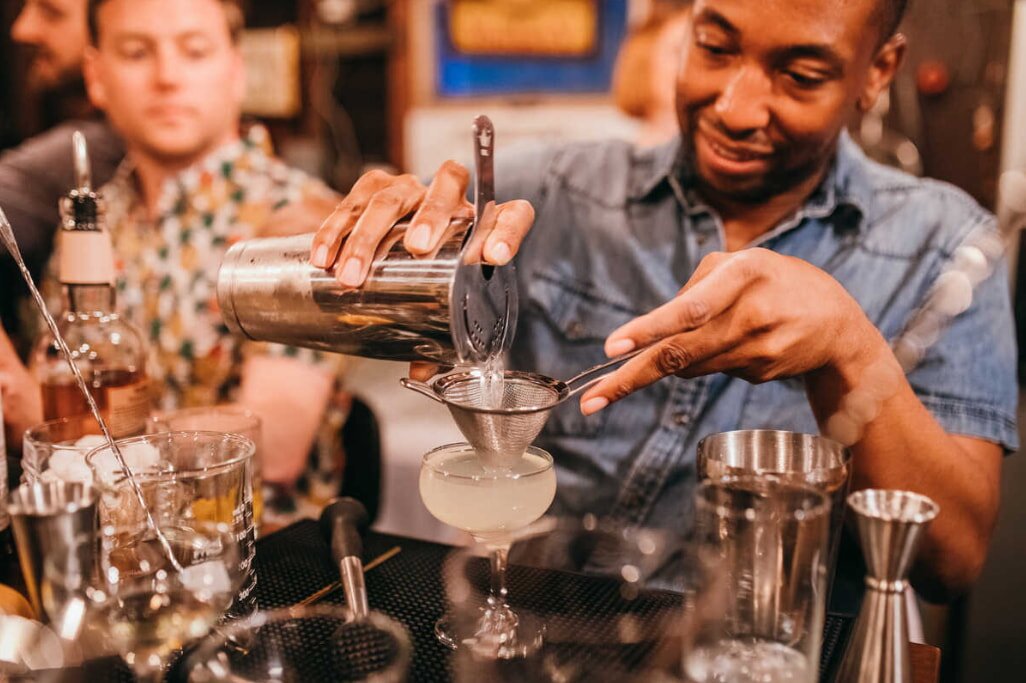 Bartender pouring cocktail through strainer into glass