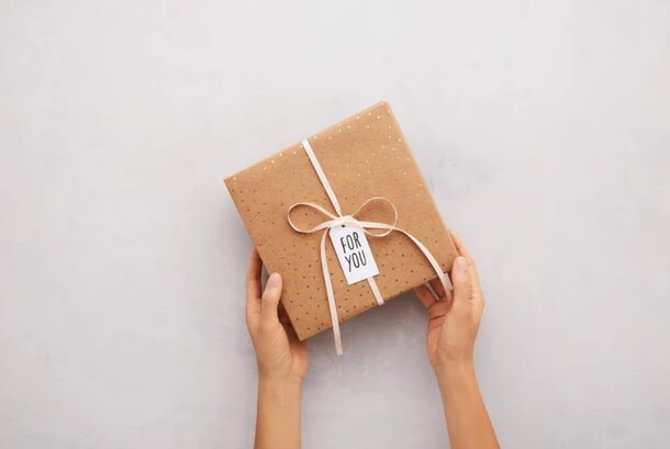 Hands gently hold a brown gift wrapped in textured brown paper, showcasing a simple and elegant presentation.