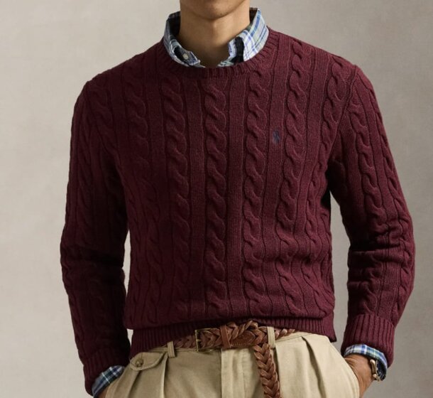A man wearing a sweater and pants stands casually, showcasing a relaxed and comfortable style.
