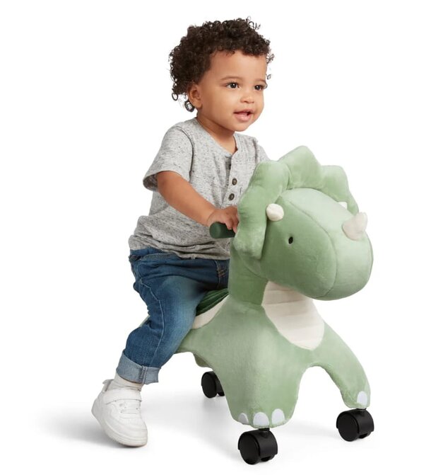 A toddler joyfully rides a bright green dinosaur toy, smiling as they play.