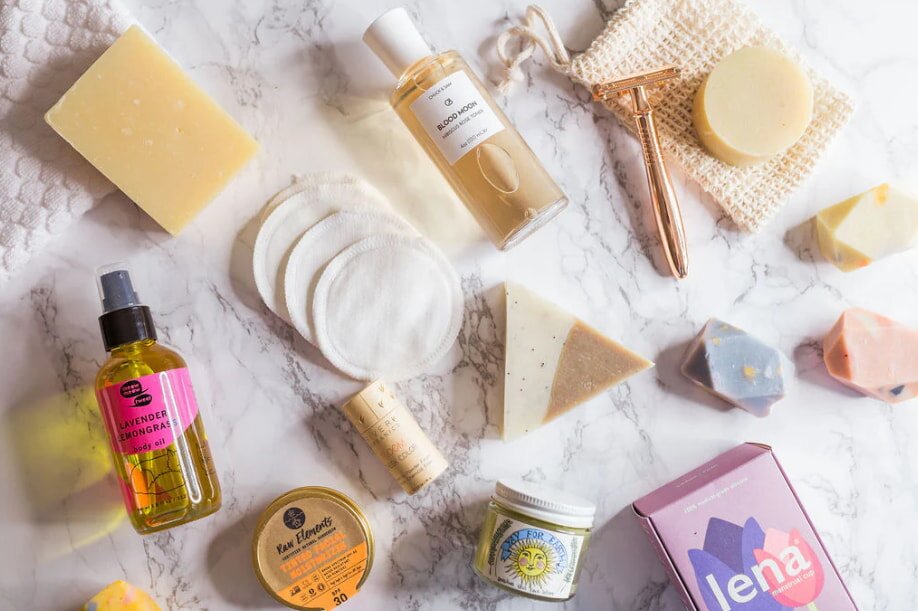 Assorted skincare and personal care products arranged on a marble surface, including bottles, bars of soap, a gold razor, and cotton pads, conveying a calm, natural vibe.