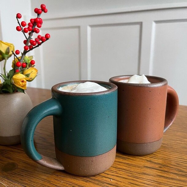 Two mugs topped with whipped cream are placed on a wooden table, creating a cozy and inviting atmosphere.