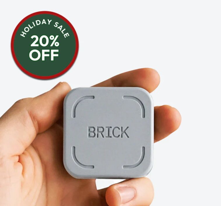 A hand holds a small, square grey item labeled "BRICK" against a white background. A red circular badge in the corner reads "Holiday Sale 20% Off.”