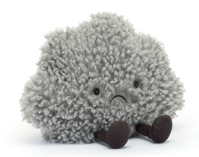 A sad-faced stuffed cloud sitting on the floor, conveying a sense of melancholy and softness.
