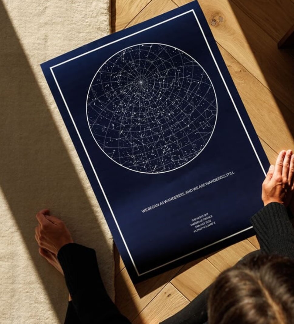 A woman sits on the floor, studying a detailed map of the night sky, surrounded by stars and constellations.