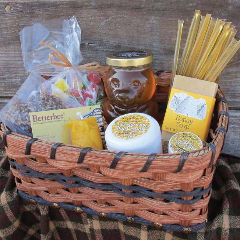 Gift basket with a honey theme, featuring a bear-shaped honey jar, honey soap, beeswax candle, moisturizing cream, and honey sticks on a plaid fabric.