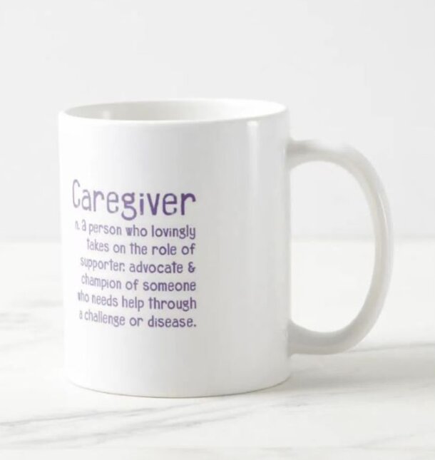 White mug on a marble surface with purple text reading "Caregiver: n. a person who lovingly takes on the role of supporter, advocate & champion."