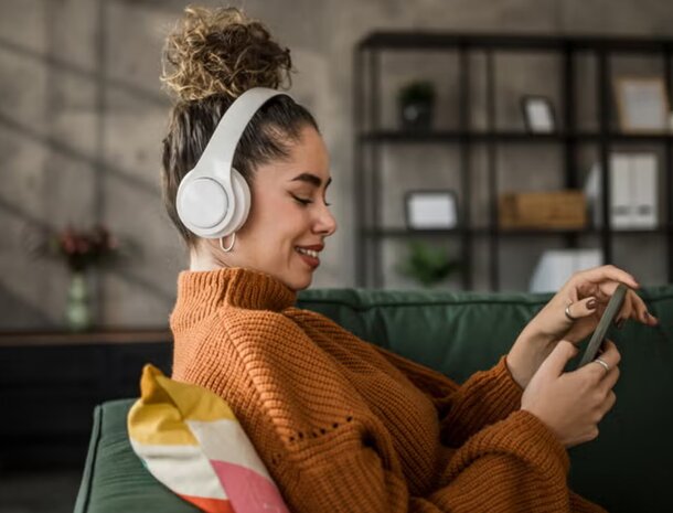 A woman with headphones sits on a couch, focused on using a tablet computer.