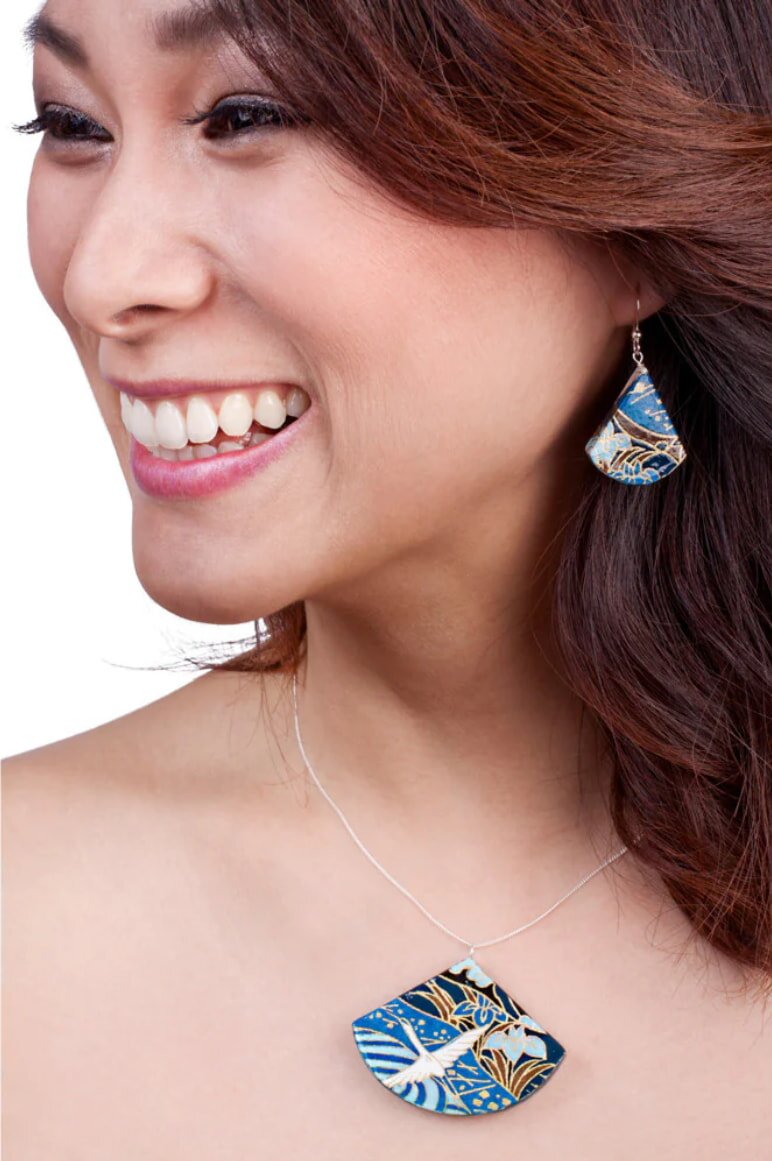 A woman with a bright smile wears a necklace adorned with a blue and white pattern, reflecting her style and happiness.