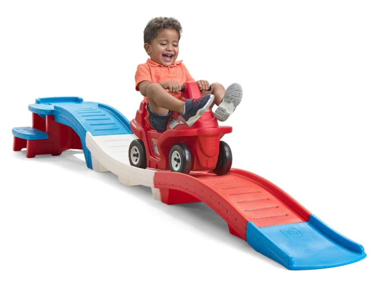 A young boy happily riding a red and blue toy car, enjoying a playful moment outdoors.