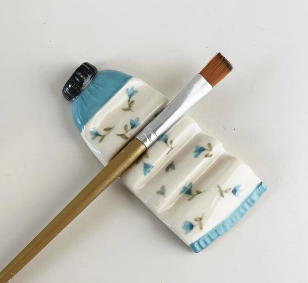 A paintbrush rests beside a decorative bottle adorned with colorful flowers.
