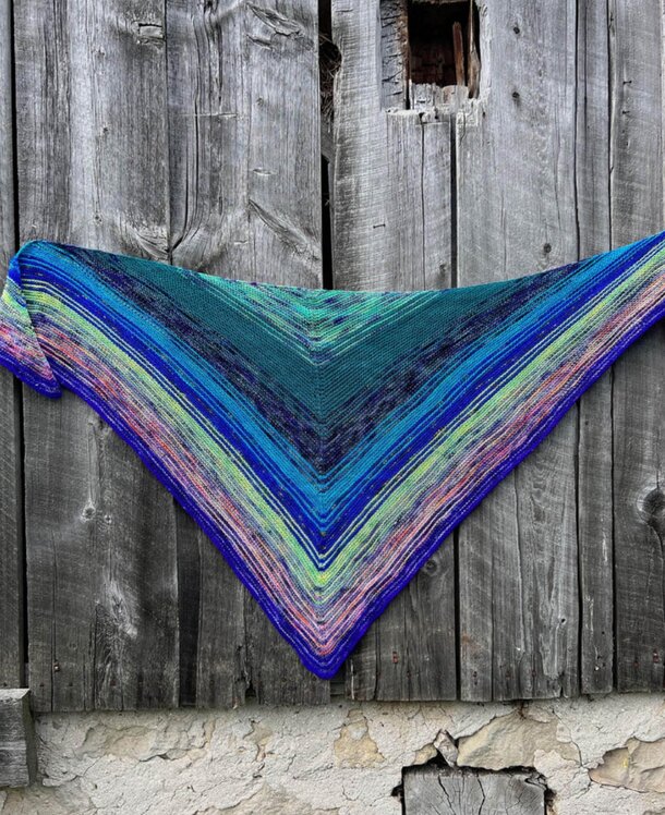 A knitted triangle shawl displayed against a rustic wooden wall, showcasing its intricate patterns and textures.