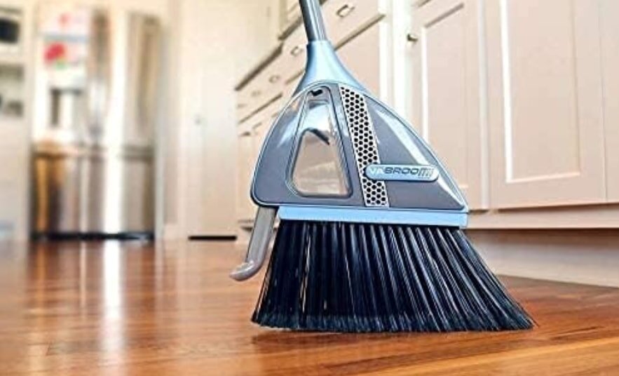 A broom resting on a hardwood kitchen floor, ready for cleaning tasks.