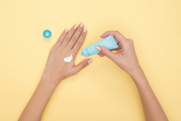 Woman's hands applying cream against a bright yellow background, highlighting skincare and beauty.