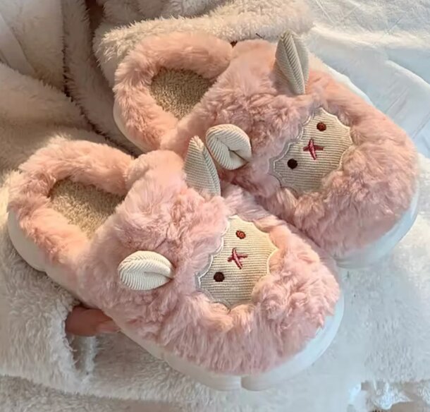 A person holds a pair of pink slippers featuring a cute rabbit face design.