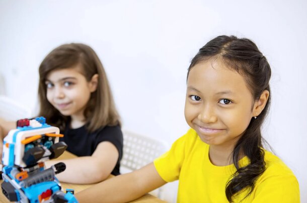 Two smiling girls hold a colorful toy robot, showcasing their joy and friendship in a playful moment.