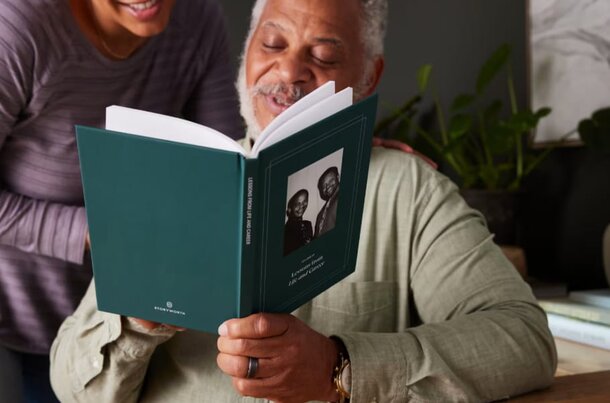 A senior couple sits closely together, reading a book and sharing smiles in a cozy, well-lit room.