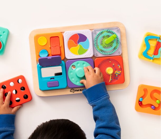 A child focused on assembling pieces of a colorful toy puzzle board on a table.