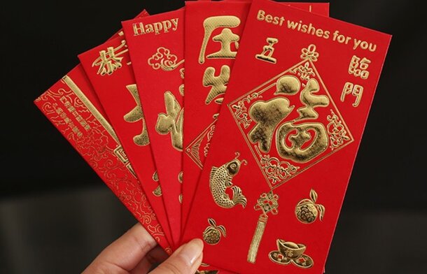 A hand holds six red envelopes with gold Chinese characters and symbols, conveying good luck and prosperity. The envelopes display festive designs.