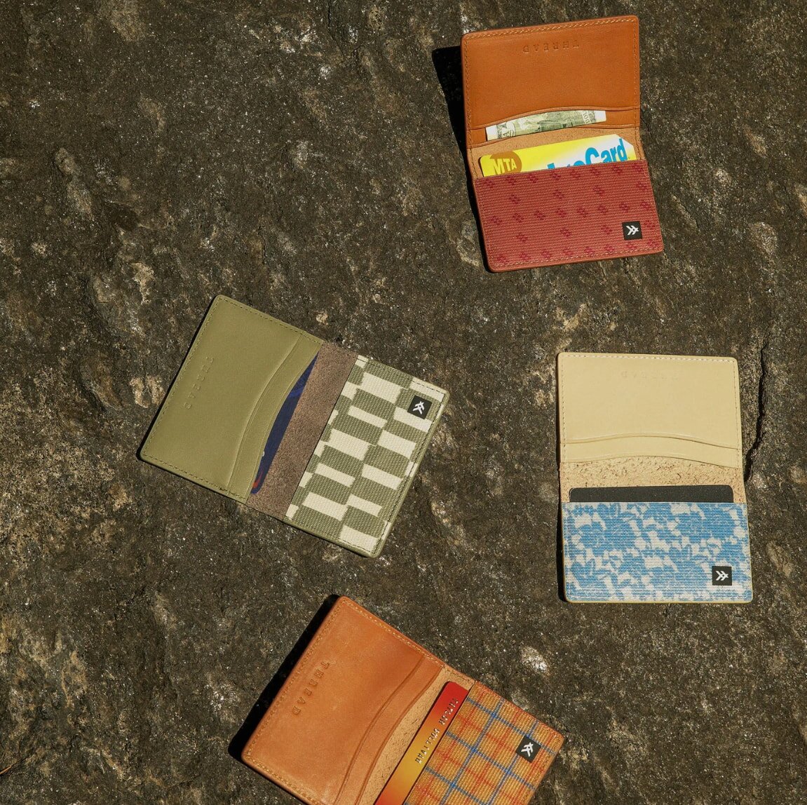 Three distinct wallet styles displayed on a textured stone surface, showcasing various designs and materials.