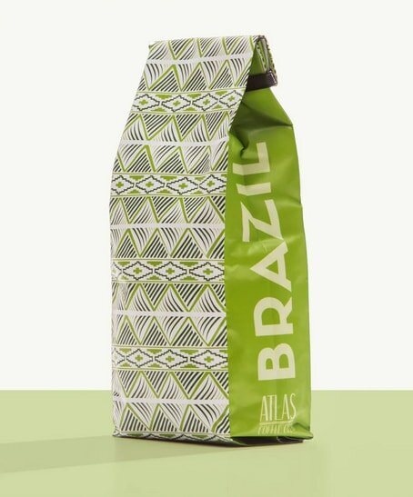 Green and white coffee bag labeled "Brazil" with geometric patterns, standing upright on a matching green surface.
