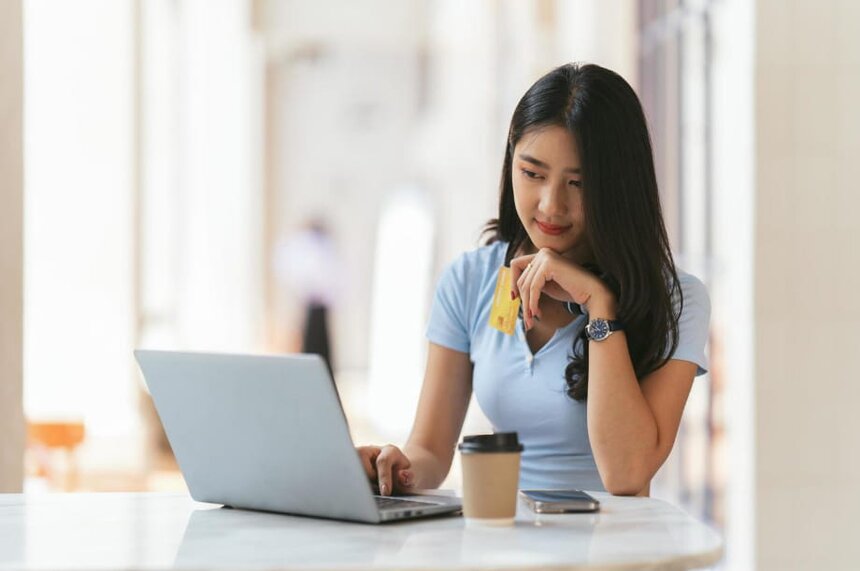 A woman seated at a table, working on a laptop with a coffee cup beside her.