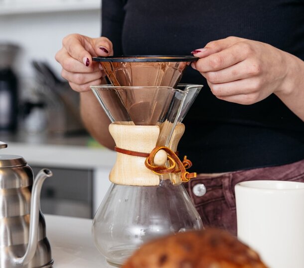 A woman pours coffee into a glass coffee maker, focusing on the brewing process in a cozy kitchen setting.