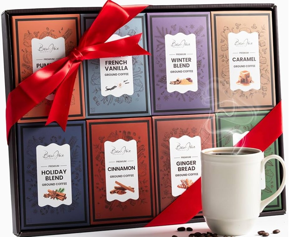 Gift box of flavored ground coffee packs, adorned with a red ribbon. Varieties include Pumpkin, Vanilla, and more. A steaming mug is in the foreground.