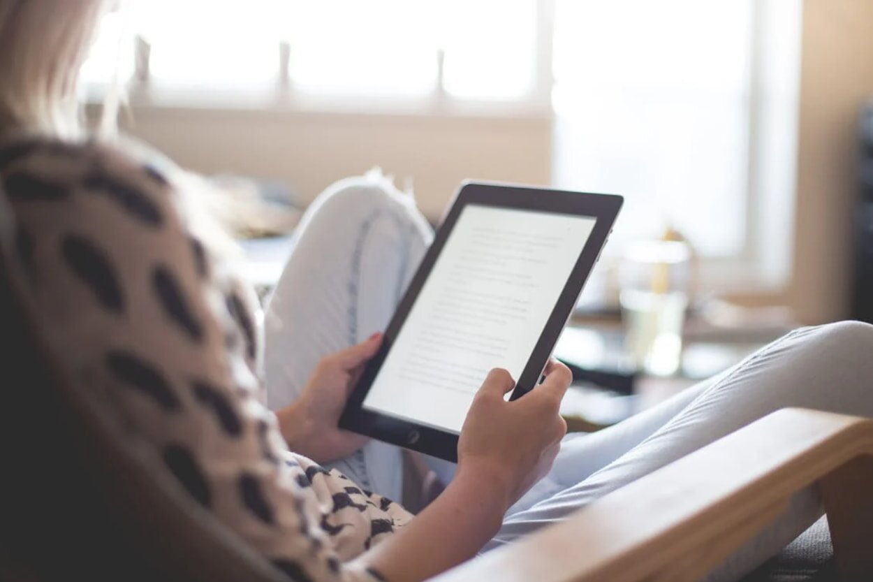 A woman sits in a chair, focused on a tablet computer in her hands.