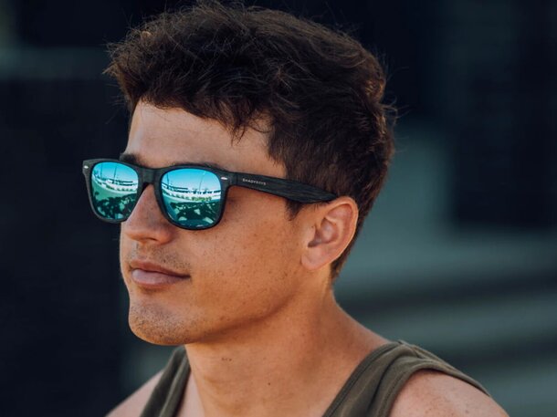 A man in sunglasses, reflecting a vibrant cityscape in the lenses, stands against an urban backdrop.