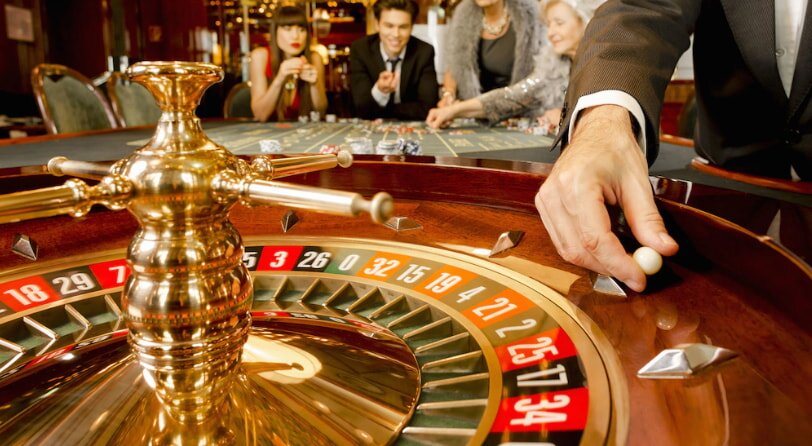 A casino table featuring a roulette wheel, surrounded by several people engaged in gameplay.