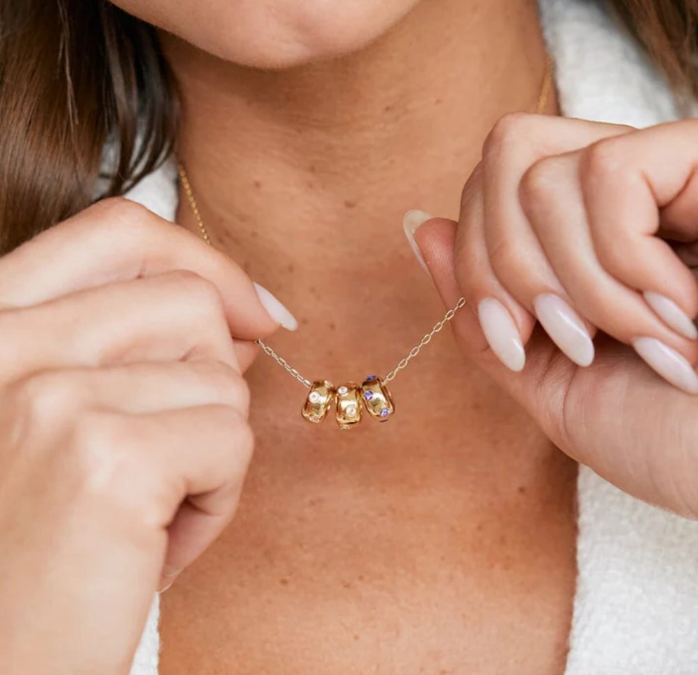 A woman holds a gold necklace featuring three sparkling diamonds, showcasing its elegance and beauty.