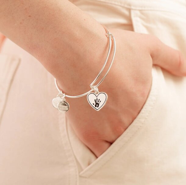 A woman's hand delicately holds a bracelet featuring a heart charm, showcasing elegance and affection.