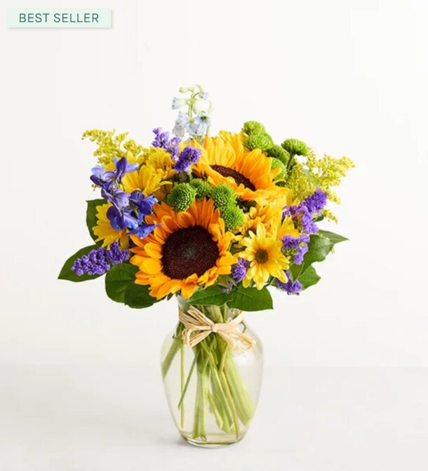 A vase filled with vibrant sunflowers alongside purple and blue flowers, creating a colorful floral arrangement.