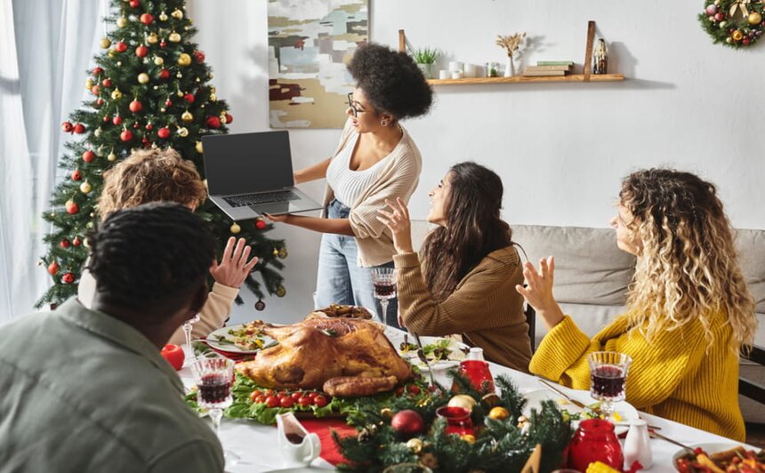A group of people gathered around a Christmas tree, engaging with a laptop on a festive occasion.